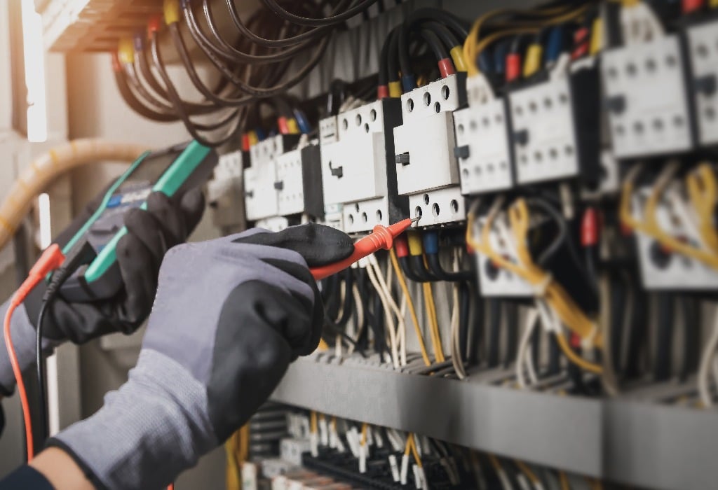 Electricity and electrical maintenance service, Engineer hand holding AC multimeter checking electric current voltage at circuit breaker terminal and cable wiring main power distribution board.